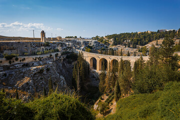 Scenic view of Gravina in Puglia, Italy, showcasing historic stone architecture, the iconic Roman bridge over the ravine, and the picturesque old town under a clear blue sky.