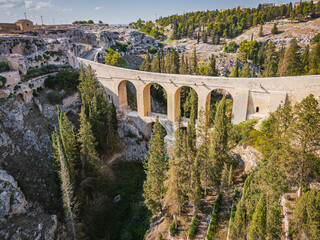 Scenic view of Gravina in Puglia, Italy, showcasing historic stone architecture, the iconic Roman bridge over the ravine, and the picturesque old town under a clear blue sky.