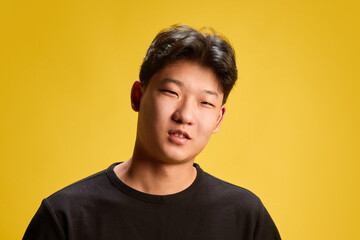 Smiling young man tilting head slightly with confident attitude against warm yellow backdrop. Concept of self-expression, style, youth culture, personality, emotions, fashion, modern lifestyle.