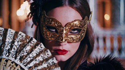 Woman wearing gold mask and holding fan. Scene is mysterious and alluring