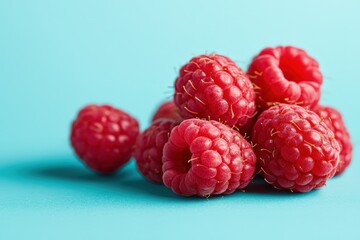 Fresh raspberries are piled together on a light blue background