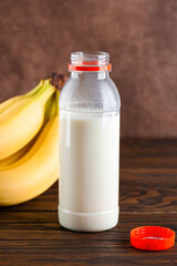 Banana milk in a bottle with bananas on a wooden table. Traditional Korean drink. Vertical orientation.