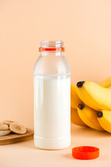 Banana milk in a bottle with bananas on a beige background. Traditional Korean drink. Vertical orientation.