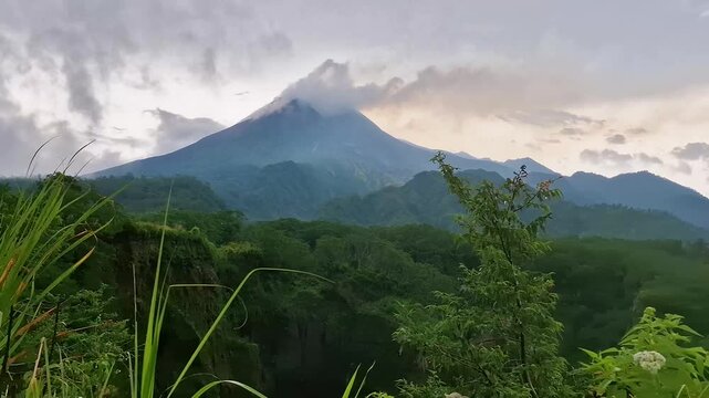 Time lapse of mount merapi in Yogyakarta, Indonesia with clouds and fog around it in the afternoon. Time lapse moment of a volcano covered in clouds with a foreground of hills and ravines