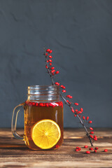 Barberry tea with lemon in a glass jar cup, branches with berries on a wooden table.
