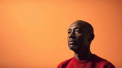 Obraz premium Thoughtful Man Looking Up with Red Sweater Against Orange Background