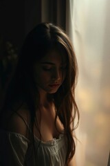 Fototapeta premium Woman Looking Down Near Window with Thoughtful Expression in Soft Light