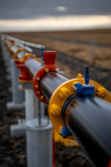 Piping and Connection:  A detailed view of a black pipeline with bright yellow, blue and red connector points stretching across a vast, open landscape under a cloudy sky.