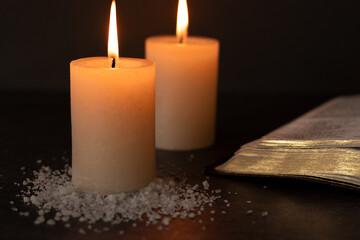 Salt and candles burning in darkness with open holy bible book. Close-up. Copy-space. Christian...