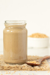 Glass jar of tahini butter with sesame seeds on table with white background. Close-up. Copy space.