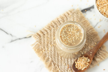 Tahini with roasted sesame seeds in a jar on white marble table. Top view. Copy space.