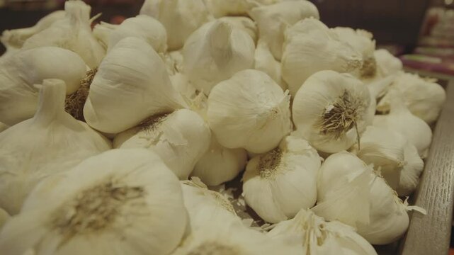 Fresh garlic bulbs neatly arranged on a grocery store shelf, showcasing their white papery skin and firm texture in a well-lit retail environment