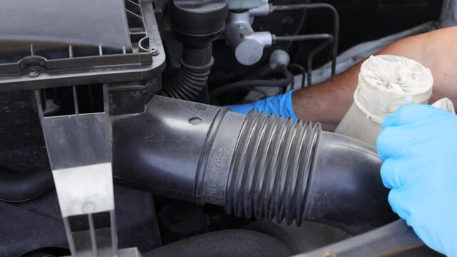 Auto mechanic wearing blue gloves, inspecting engine parts for maintenance and repair near an open vehicle hood.  Fixing vehicle cooling system.