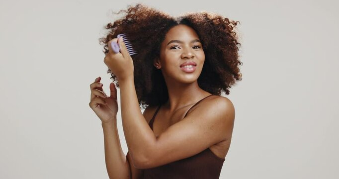 Comb, hair and face of black woman in studio for wellness, healthy texture and natural growth. Hairdresser, salon and portrait of person with confidence, beauty and curly style on white background