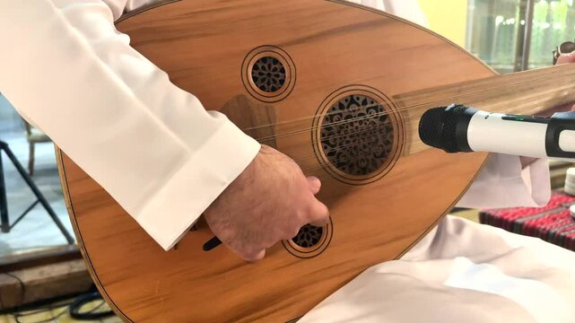 Oud instrument captures Arabic musical essence as fingers glide across carved wood, microphone nearby records every note for tourist seeking authentic culture and exclusive vacation tradition.
