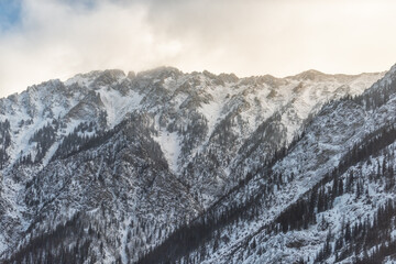 Snow covered Gore mountain range in morning sunrise clouds and blue sky with jagged peaks and trees