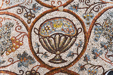 Detailed ancient Roman mosaic featuring a decorative fruit basket, intricate floral patterns, and vibrant tesserae on a floor of ruined ancient church in Hurvat Beit Loya, Israel