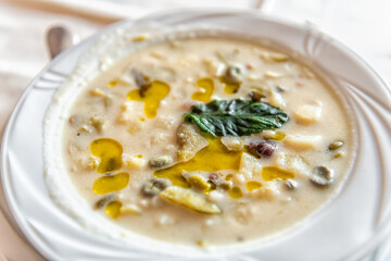 Sardinian vegetable soup local minestrone with green broad fava beans, potato, fregola pasta, bacon cubes, mint leaves in white bowl at Sardinia Italy