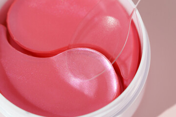 Close-up of white jar with pink hydrogel eye patches and spatula on pink isolated background. Concept of natural moisturizing beauty products, wrinkle filling, skin tightening, dark circles reduction