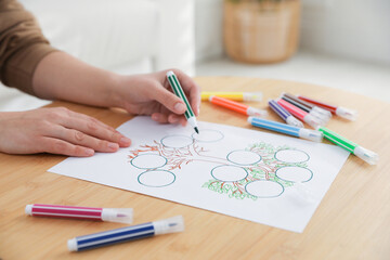 Woman drawing family tree at wooden table, closeup