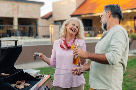 Senior couple grilling meat and having drinks in backyard