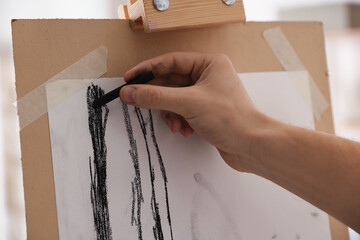 Young man painting picture with black wax crayon in artist's studio, closeup