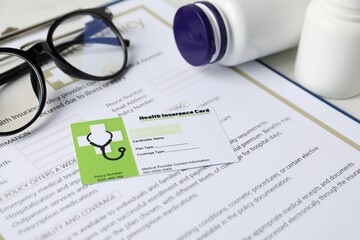 Health insurance card, policy and medical bottles on white table, closeup