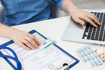 Doctor with medical insurance card and policy working on laptop at white table, closeup