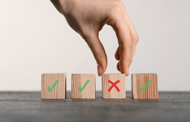 Rejected. Woman choosing cube with cross among other ones with check marks at table, closeup