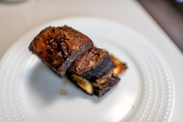 Beef rib grass-fed piece cooked baked roasted meat bone crispy homemade food on white plate macro closeup on table