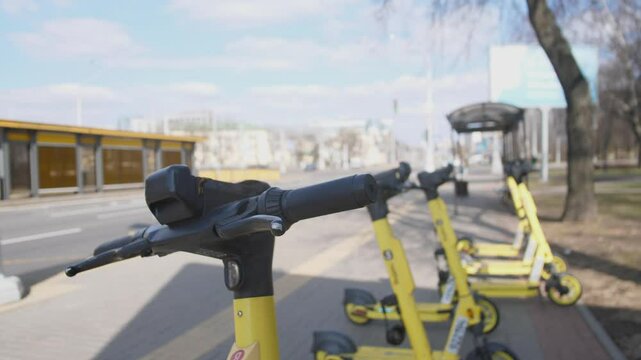 A row of bright yellow electric scooters is readily available for rent along a bustling city street under clear skies