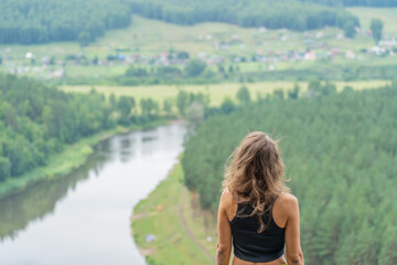 Rear view of a hiker woman admiring a serene river and lush green valley while standing atop a breathtaking mountain