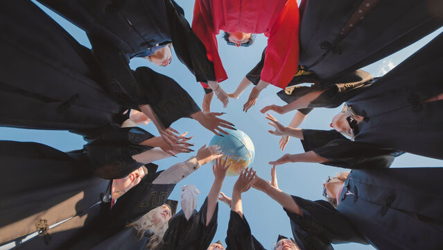 Graduates in academic gowns reaching for a globe, representing global collaboration and citizenship