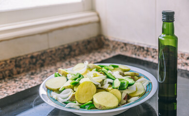 A green bottle of olive oil sits on a counter next to a plate of food. The plate is filled with a variety of vegetables, including potatoes, onions, and peppers. Concept of health and wellness