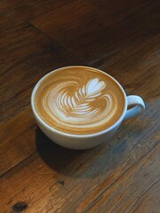 Cup of coffee on wooden table. A flat white in on a wooden table. Specialty coffee with arte latte. Real arte latte.
Minimalist flat white coffee with latte art and shadow on white table, top-down.