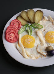 Plate of fried eggs served with pickles, tomatoes, olives and green peppers, top view of breakfast meal captured in clean lighting for food styling, restaurant menu, cooking concept or nutrition