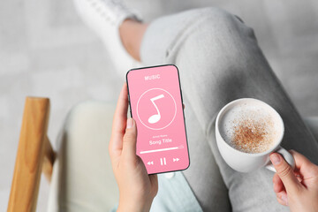 Woman using mobile phone to listen to music indoors, closeup. Open music player app on device screen