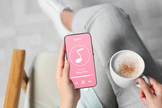 Woman using mobile phone to listen to music indoors, closeup. Open music player app on device screen