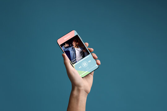 Man showing mobile phone with open music player app on blue background, closeup