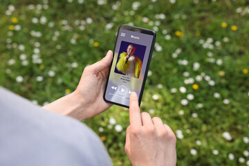 Woman using mobile phone to listen to music outdoors, closeup. Open music player app on device...