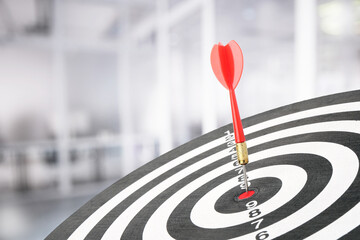 Targeting and business success. Dart sticking in center of dartboard in office, closeup