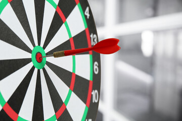 Targeting and business success. Dart sticking in center of dartboard in office, closeup