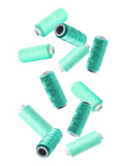Spools of turquoise sewing threads falling on white background