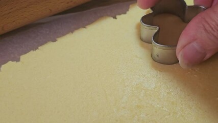 A baker cuts cookie dough into gingerbread man shapes using a metal cutter. A wooden rolling pin and parchment paper set the scene for holiday baking at home. - Powered by Adobe