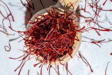 Naklejka premium red Saffron threads in wood spoon spilling on white marble background, light and airy with sunlight and shadows, top down view