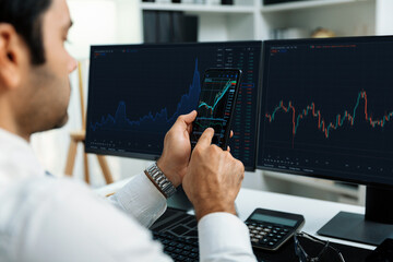 Trader businessman searching on smartphone, analyzing in dynamic stock exchange investment screen on pc with invest highest profitable financial technology market at modern home office. Surmise.