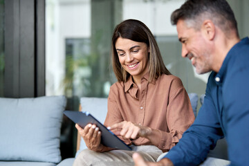 Two happy professional business colleagues working using digital tablet and talking sitting in...
