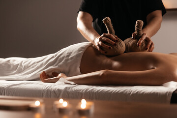 Healing herbal massage. Relaxed woman enjoying body massage with herbal compress balls in calm spa...