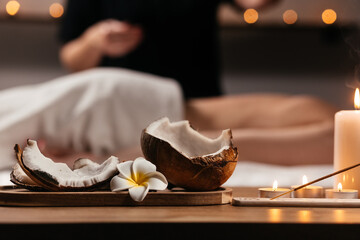 Spa and treatment setting with aroma stick, candle light, coconut and Frangipani Leelawadee flower on wooden table. Spa decoration against blurred background with female relaxing during massage
