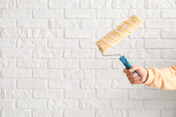Worker with paint roller on white brick background